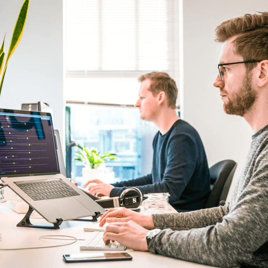 Two men sitting at a desk working on a laptop